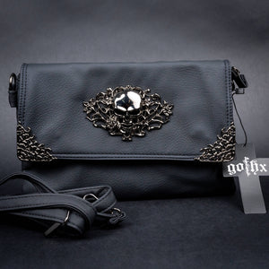 A black vegan leather bag by CHOK GothX with a metallic skull and rose detailing on the front flap, styled on a black backdrop with the gothx tag showing. The detachable adjustable strap is shown in front.