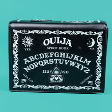 Load image into Gallery viewer, The GothX Ouija Spirit Book Mini Bag sat on a teal background. The bag is forward to highlight the ouija spirit book white printed detailing on the black book bag with the 3D planchette stitching. Bag is inspired by witchy style and necromancy.
