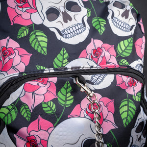 Close-up of chain and front pocket with floral skull pattern – A close-up of the chain accessory attached to the zipper on the front pocket, with a clear view of the white skulls, pink roses, and green leaves pattern on a black background.