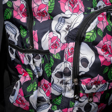 Load image into Gallery viewer, Front view of skull and rose print backpack – A gothic backpack with a striking black background, adorned with white skulls and vibrant pink roses with green leaves. The front has a zip pocket and a silver chain detail, adding an edgy touch to the design.
