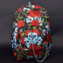 Load image into Gallery viewer, Front view of blue skull and red rose print backpack – A bold, gothic backpack with a black background featuring blue skulls, vibrant red roses, and golden vines. The front includes a zip pocket and a silver chain detail for an edgy, alternative look.
