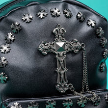Load image into Gallery viewer, A close up of the GothX black cross vegan stud mini backpack on a teal background. The vegan leather bag is facing forwards to highlight the cross studs along the top zip line and top of zipped pocket, studded cross with chain centrepiece and side metal cross studs on the slot pockets.
