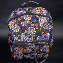 Load image into Gallery viewer,  A vibrant backpack featuring a lively sugar skull design with bright colours, including red, yellow, blue, and purple flowers on a black background. The front zip pocket has a silver chain detail, adding a unique touch to the festive look.
