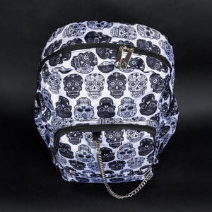 Front view of a gothic sugar skull backpack by CHOK GothX. This white bag with black skull prints is equipped with multiple compartments and silver chain embellishment, combining practical storage with a striking alternative aesthetic.