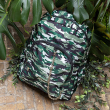 Load image into Gallery viewer, Classic Camouflage vegan backpack with chain sat outside in front of a tropical plant and brick wall. The backpack with a green and brown camo print is facing forward highlighting the two front zip pockets, two side pockets and silver decorative chain.
