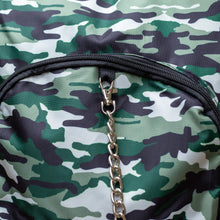 Load image into Gallery viewer, Close up of the Classic Camouflage vegan backpack with chain hanging on a brick wall. The backpack with a green and brown camo print is facing forward highlighting the two front zip pockets, two side pockets and silver decorative chain.
