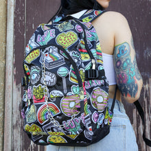 Load image into Gallery viewer, The kawaii graffiti doodle vegan backpack being worn by a tattooed model in front of a brown painted wall. The bag is facing forward to highlight the two front zip pockets, two elastic side pockets &amp; silver chain. The all over print has lollipops, pugs, rainbows, pizzas, polaroid cameras, eyes and fries.
