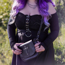Load image into Gallery viewer, Model wearing a goth outfit holding the gothx don&#39;t cross me vegan shoulder bag across their body with the bag facing forward to highlight the studded cross chain centrepiece.
