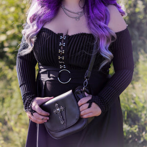 Model wearing a goth outfit holding the gothx don't cross me vegan shoulder bag across their body with the bag facing forward to highlight the studded cross chain centrepiece.
