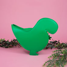 Load image into Gallery viewer, The kawaii green glitter dino vegan bag on a pink studio background with green foliage. The bag is facing away from camera to highlight the detachable strap and plain green back.
