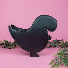 Load image into Gallery viewer, The kawaii black glitter dino vegan bag on a pink studio background with green foliage surrounding it. The bag is facing away from the camera to highlight the plain black back and detachable strap.
