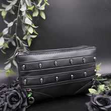Load image into Gallery viewer, The gothx mini skull head vegan clutch bag on a black studio background with black roses and green leaf foliage surrounding it. The clutch is facing forward to highlight the skull studded front and faux zip detailing.
