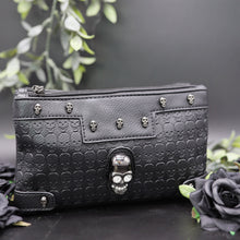 Load image into Gallery viewer, The gothx crystal skull vegan clutch bag on a black studio background with black roses and green foliage surrounding it. The bag is facing forward to highlight the embossed skull vegan black leather, mini skull studs, two main zip compartments and crystal skull centrepiece.
