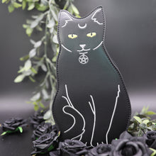 Load image into Gallery viewer, The gothx pagan black cat vegan shoulder bag on a black studio background with green foliage and black roses surrounding it. The bag is facing forward to highlight the embroidery details including a pentagram collar, yellow eyes and paws. 
