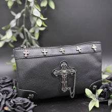Load image into Gallery viewer, The gothx don&#39;t cross me vegan clutch bag on a black studio background with black roses and green foliage surrounding it. The clutch is facing forward to highlight the cross studs and stud, chain cross centrepiece.
