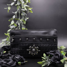 Load image into Gallery viewer, The gothx black skull vegan clutch bag on a black studio background with black roses and green foliage surrounding it. The clutch is facing forward to highlight the skull embossed vegan black leather, the crystal stud skull centrepiece, zip pocket and skull studs.
