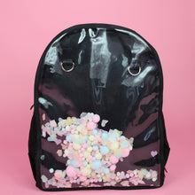 Load image into Gallery viewer, The Kawaii Black &amp; Clear Window Vegan Ita Backpack on a pastel pink background. The bag is facing forward filled with pastel confetti and pom poms to highlight the clear display window and inside D rings to hang things from.
