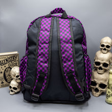 Load image into Gallery viewer, The Purple Checkerboard Backpack sat on a grey background with a palmistry guide book and two skull stack on the right and a phrenology guide candle and three skull stack on the left. The vegan friendly bag is facing away from the camera to highlight the plain black back, the two side elasticated pockets, the top handle and the two adjustable padded shoulder straps.
