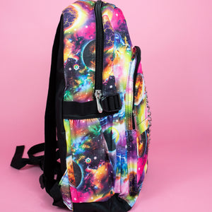 The pink and purple space galaxy vegan backpack sat on a pink studio background. The backpack is facing right to highlight the multicoloured space/planet/galaxy print, two zip pockets, two elastic side pockets and detachable silver chain.