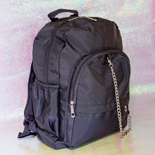 Load image into Gallery viewer, The black nylon vegan backpack with chain on an iridescent background. The bag is facing forward angled right to highlight the two front zip pockets, two side pockets, double zip main compartment, top handle and detachable silver chain.
