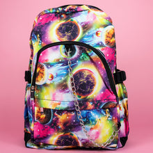 Load image into Gallery viewer, The pink and purple space galaxy vegan backpack sat on a pink studio background. The backpack is facing forward to highlight the multicoloured space/planet/galaxy print, two zip pockets, two elastic side pockets and detachable silver chain.
