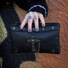 Load image into Gallery viewer, The gothx don&#39;t cross me vegan clutch bag being held by a tattooed model in front of a graffiti wall. The clutch is facing forward to highlight the cross studs and stud, chain cross centrepiece.
