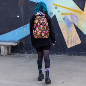 Model walking away wearing the floral gold skull nylon chain vegan backpack. The bag is facing the camera to highlight the flowers and skulls print, two zipped pockets, two elastic side pockets and detachable decorative silver chain.