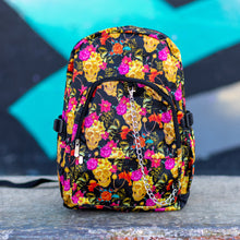 Load image into Gallery viewer, The floral gold skull nylon chain vegan backpack sat on a skatepark bench. The bag is facing forward to highlight the flowers and skulls print, two zipped pockets, two elastic side pockets and detachable decorative silver chain. 
