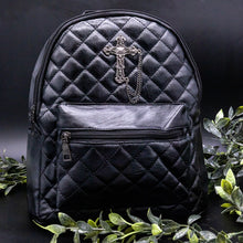 Load image into Gallery viewer, The GothX quilted cross vegan mini backpack on a black studio background with black roses and leaves surrounding it. Quilted front detailing with a studded cross with hanging chain appliqué and zip front pocket. Black vegan leather with gunmetal grey detailing. The bag is facing forward to show off the front details.
