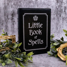 Load image into Gallery viewer, The gothx little book of spells vegan shoulder bag on a grey background with green foliage and gold frames surrounding it. The bag is facing forward sat upright to highlight the white print detailing on the front and spine.
