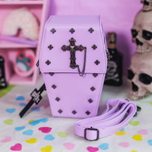 Load image into Gallery viewer, The GothX Pastel Lilac Mini Coffin Vegan Cross Body Bag on a pastel purple background with pastel pink coffin shelving, skulls and black faux skull poison bottles in the background. The bag is facing forward to highlight the cross studs, cross &amp; chain centrepiece, detachable chain and detachable adjustable shoulder strap.
