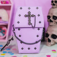 Load image into Gallery viewer, The GothX Pastel Lilac Mini Coffin Vegan Cross Body Bag on a pastel purple background with pastel pink coffin shelving, skulls and black faux skull poison bottles in the background. The bag is facing forward to highlight the small cross studs, cross and chain centrepiece and detachable decorative chain.
