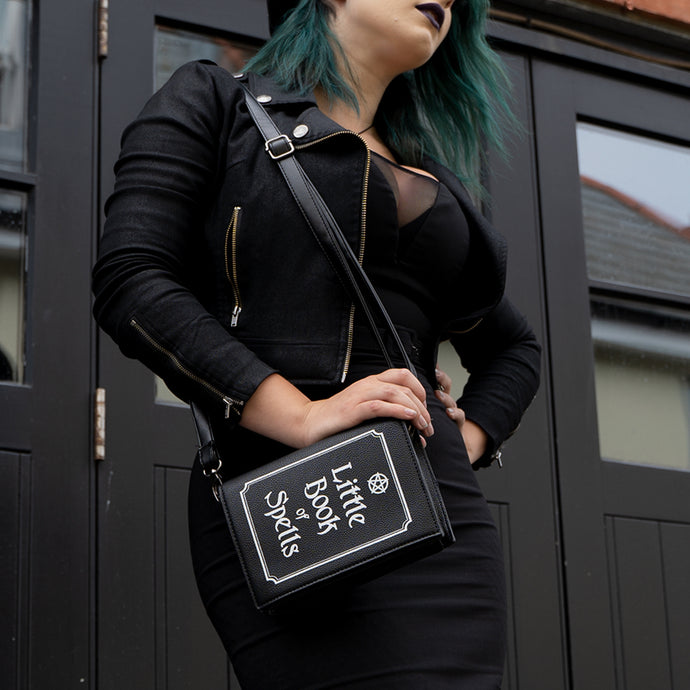 Model wearing an all black goth style outfit holding the gothx little book of spells vegan shoulder bag on one shoulder. The witchy inspired vegan leather bag is facing towards the camera to highlight the white printed design of a pentagram, framing and text reading little book of spells.