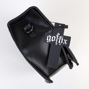 The GothX Ouija Spirit Book Mini Bag laying on its side on a white background to show the metal D ring on either side, the magnetic clip flap closure, zipped middle and plain black vegan leather side.