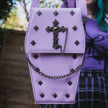 Load image into Gallery viewer, The GothX Pastel Lilac Mini Coffin Vegan Cross Body Bag being held up by a gothic alternative model. The vegan friendly pastel leather bag is facing forward to highlight the cross studs, cross &amp; chain centrepiece, detachable chain and detachable adjustable shoulder strap.
