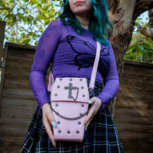 Load image into Gallery viewer, GothX Pastel Pink Mini Coffin Vegan Cross Body Bag being held up by an alternative goth model. The bag is facing forward to highlight the cross studs, cross &amp; chain centrepiece, detachable chain and detachable adjustable shoulder strap.
