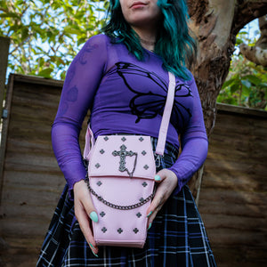 GothX Pastel Pink Mini Coffin Vegan Cross Body Bag being held up by an alternative goth model. The bag is facing forward to highlight the cross studs, cross & chain centrepiece, detachable chain and detachable adjustable shoulder strap.