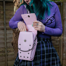 Load image into Gallery viewer, GothX Pastel Pink Mini Coffin Vegan Cross Body Bag being held up by an alternative goth model. The bag being opened up to show the magnetic clip close flap, the detachable chain and stud detailing.
