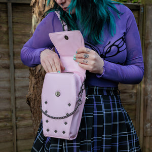 GothX Pastel Pink Mini Coffin Vegan Cross Body Bag being held up by an alternative goth model. The bag being opened up to show the magnetic clip close flap, the detachable chain and stud detailing.