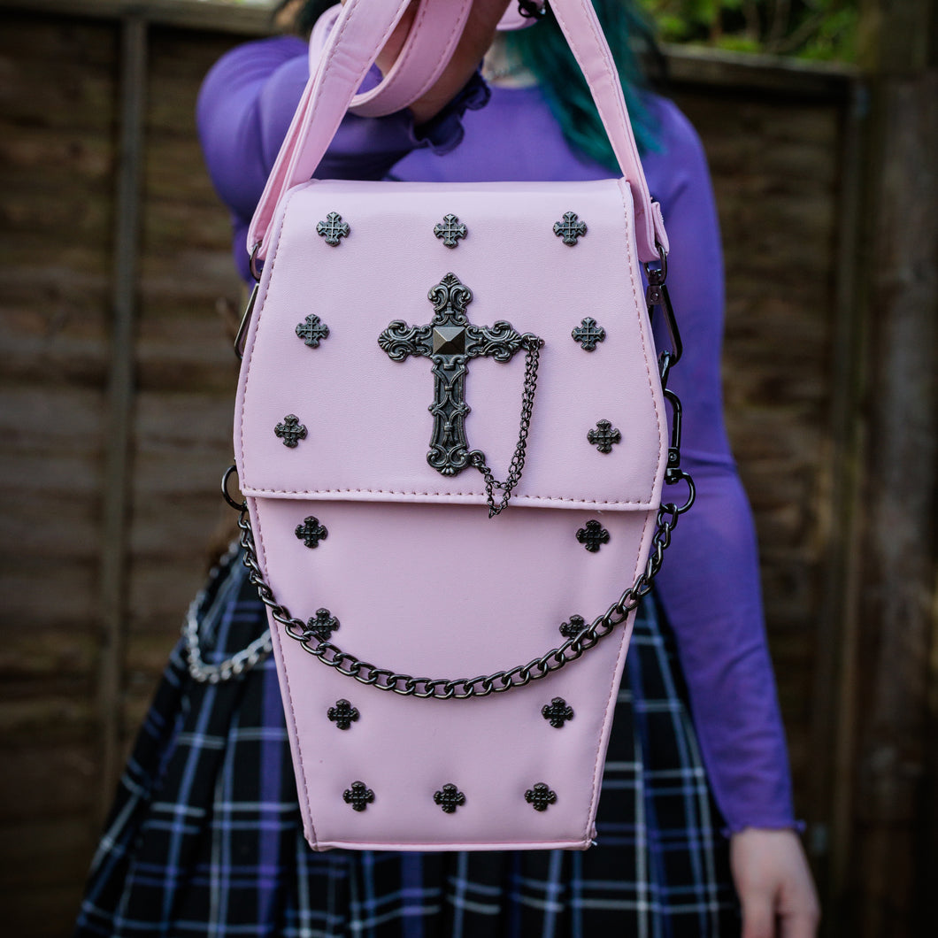 GothX Pastel Pink Mini Coffin Vegan Cross Body Bag being held up by an alternative goth model. The bag is facing forward to highlight the cross studs, cross & chain centrepiece and detachable chain.