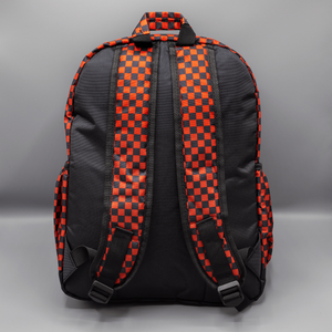 The Red Checkerboard Backpack sat on a grey background. The vegan friendly bag is facing away from the camera to highlight the plain black back, the two side elasticated pockets, the top handle and the two adjustable padded shoulder straps.
