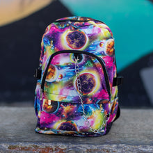 Load image into Gallery viewer, The pink and purple space galaxy vegan backpack sat on a skatepark bench. The backpack is facing forward to highlight the multicoloured space/planet/galaxy print, two zip pockets, two elastic side pockets and detachable silver chain. 
