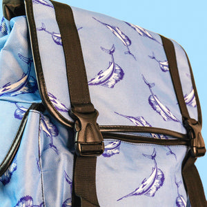 A pastel blue backpack with black buckle and strap detailing with swordfish printed all over. Close up of the black buckle close with black piping detailing.