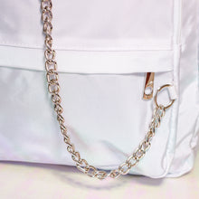 Load image into Gallery viewer, The white nylon vegan backpack with chain on an iridescent background. Close up of the detachable silver chain and front zip pocket detailing.
