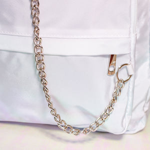 The white nylon vegan backpack with chain on an iridescent background. Close up of the detachable silver chain and front zip pocket detailing.