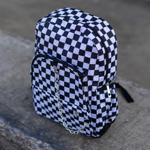 Load image into Gallery viewer, CHOK white checker vegan backpack sat on a skatepark bench. The bag is facing forward angled left to highlight the white and black checkered square print, silver detachable chain, two front zip pickets and two side elastic pockets.
