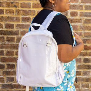 The White & Clear Window Ita Backpack being worn on a shoulder of an alternative model wearing run and fly dungarees and a black tshirt. The bag is facing forward to highlight the clear front window with two metal D rings, two side elasticated pockets, main zip compartment and top handle. The vegan friendly bag is inspired by kawaii jfashion.