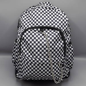 The White Checkerboard Backpack sat on a grey background. The vegan friendly bag features an all over mini black and white check print with black trim along the silver zips. The bag is facing forward to highlight the two front zip pockets, two side elasticated pockets, the top zip compartment, the top handle and the silver decorative detachable chain draping across the front.