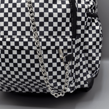 Load image into Gallery viewer, Close up of the White Checkerboard Backpack sat on a grey background. The vegan friendly bag features an all over mini black and white check print with black trim along the silver zips. The bag is facing forward to highlight the two front zip pockets, two side elasticated pockets, the top zip compartment, the top handle and the silver decorative detachable chain draping across the front.
