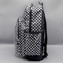 Load image into Gallery viewer, The White Checkerboard Backpack sat on a grey background. The vegan friendly bag features an all over mini black and white check print with black trim along the silver zips. The bag is facing left to highlight the two front zip pockets, two side elasticated pockets, the top zip compartment, the top handle and the silver decorative detachable chain draping across the front.
